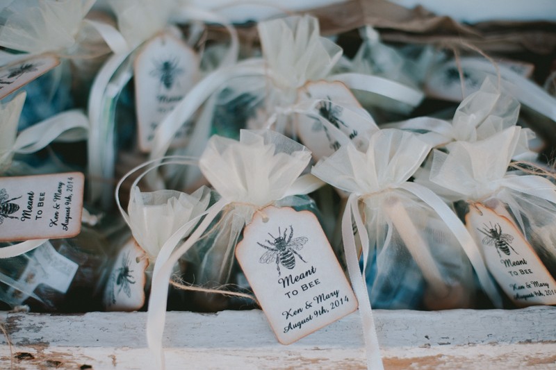 Honey wedding favors in a satchel with a honey dipper and small jar of honey, tied with a tag that says "Meant To Bee". 