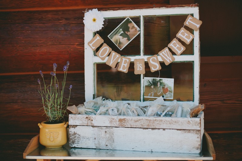 Vintage window pane with a banner that says "Love is Sweet", with a rustic trough holding wedding favors. 