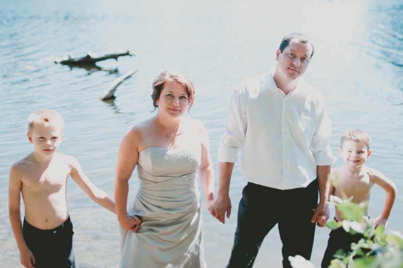 Unique bridal family portraits with bride, groom and their two sons standing in the water at Island Lake Park in Silverdale, WA. 