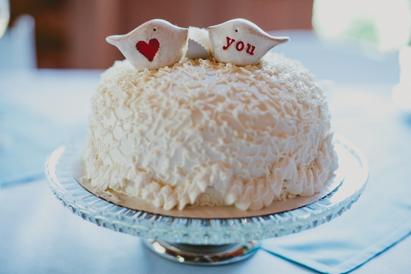 Small wedding cake with cornelli lace piping, topped with two white and red birds, on a vintage cake plate. 