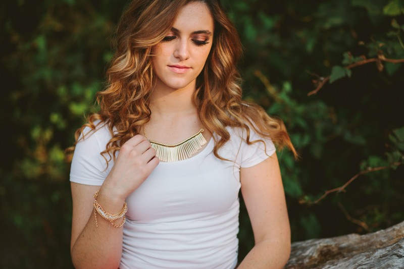 High school senior girl with a gold statement necklace, professional makeup application, and a curled hairstyle. 