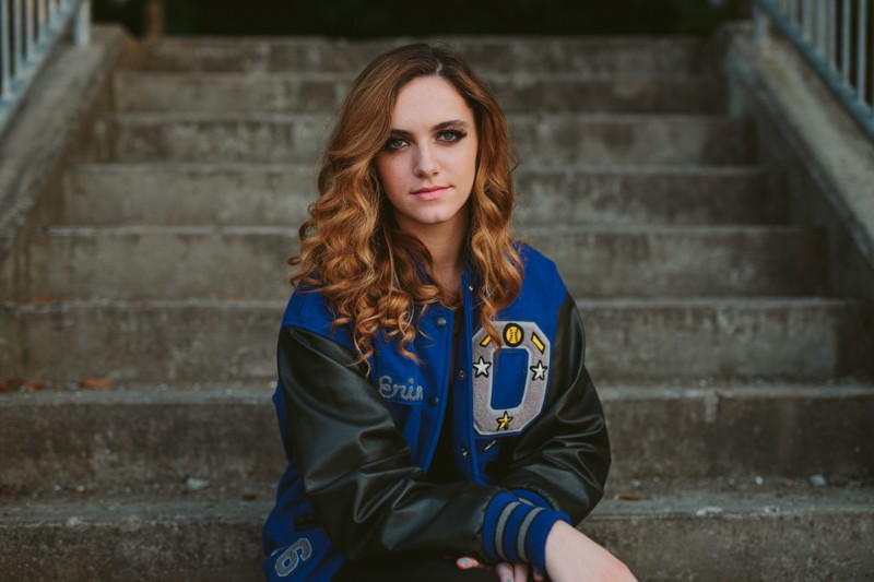 High school senior girl in a letterman jacket, with a curly hairstyle and smokey eye makeup, in Kitsap County. 