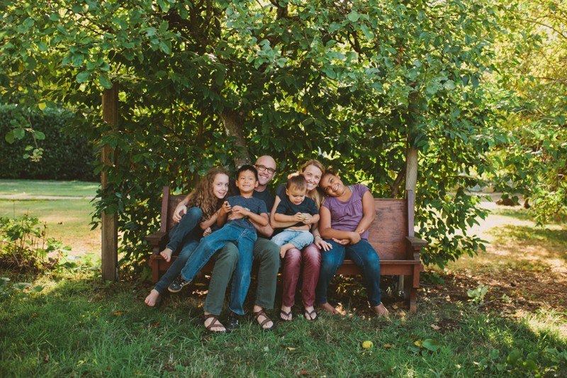 Family sitting on a vintage wooden bench in a sunny garden near Seattle. 