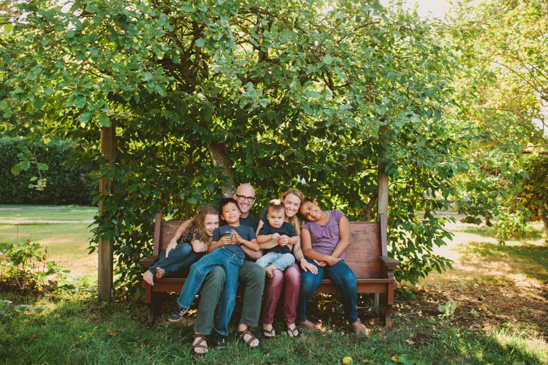 Family with children sitting under a tree in a sunny backyard, by Meghann Prouse. 