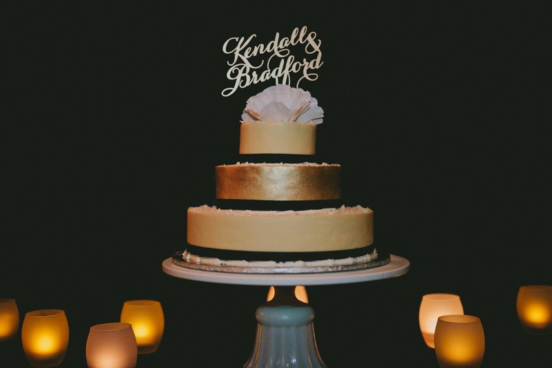 Elegant gold and black wedding cake, with a paper flower and custom laser cut topper. 