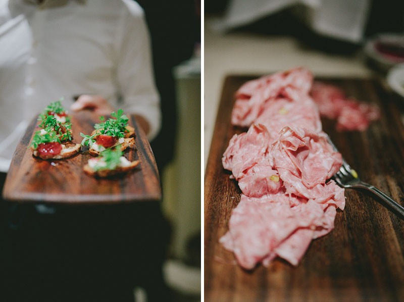 Server holding a wooden serving plank with hors d'oeuvres and prosciutto. 