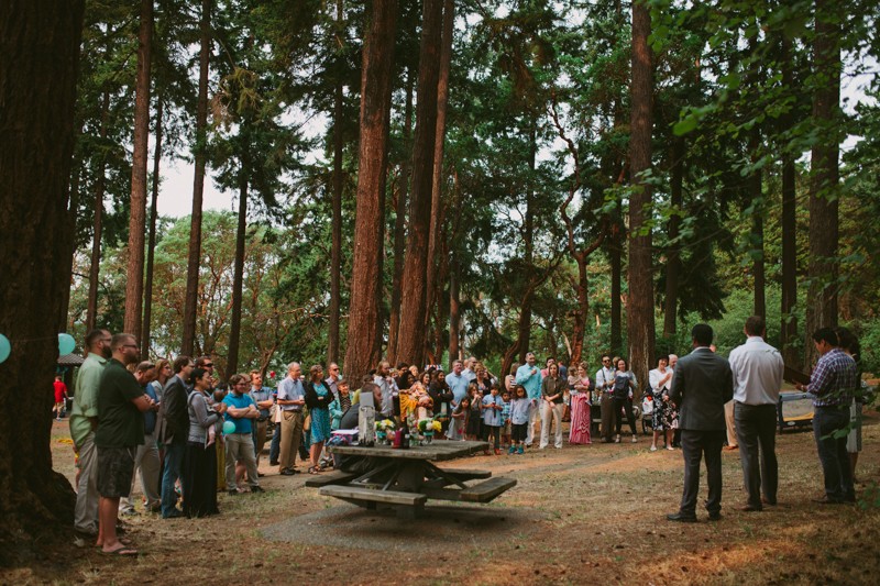 Small, woodsy wedding in West Seattle, with guests surrounded by tall trees. 