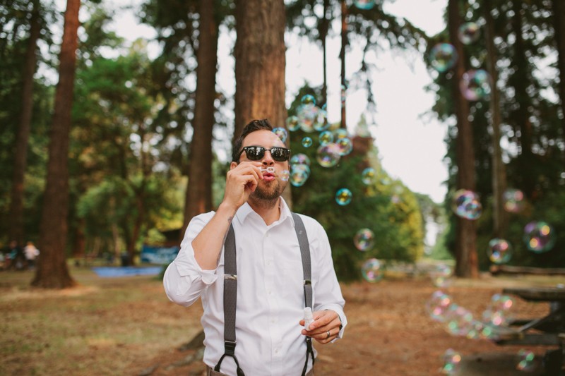 Wedding guest in suspenders and sunglasses, blowing bubbles. 