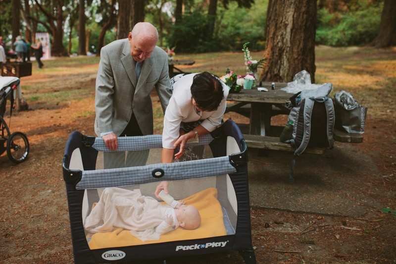 Grandparents feeding granddaughter in a playpen, at a small park wedding. 