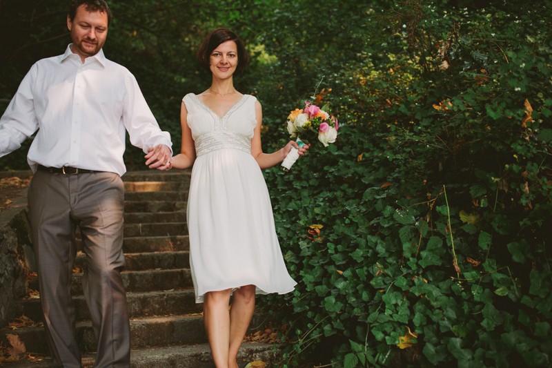 Bride and groom holding hands, walking down steps, with bride in a sweet knee-length, v-neck wedding dress. 