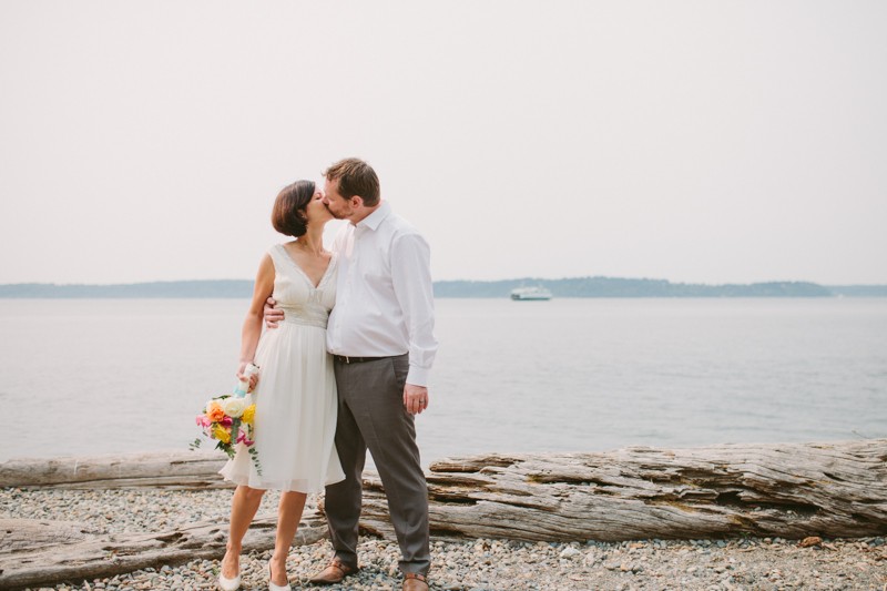 Bride and groom kissing on a beach, with a ferry in the background. 
