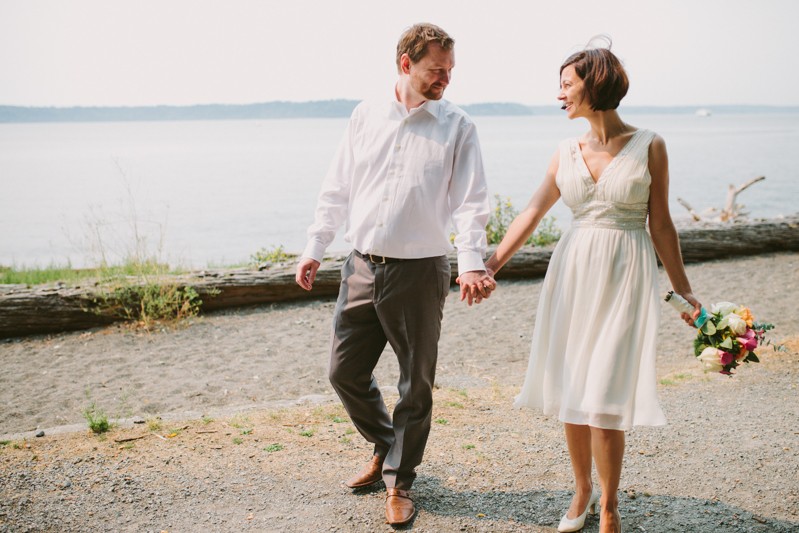 Bride and groom holding hands on a West Seattle beach, with bride in a v-neck dress. 
