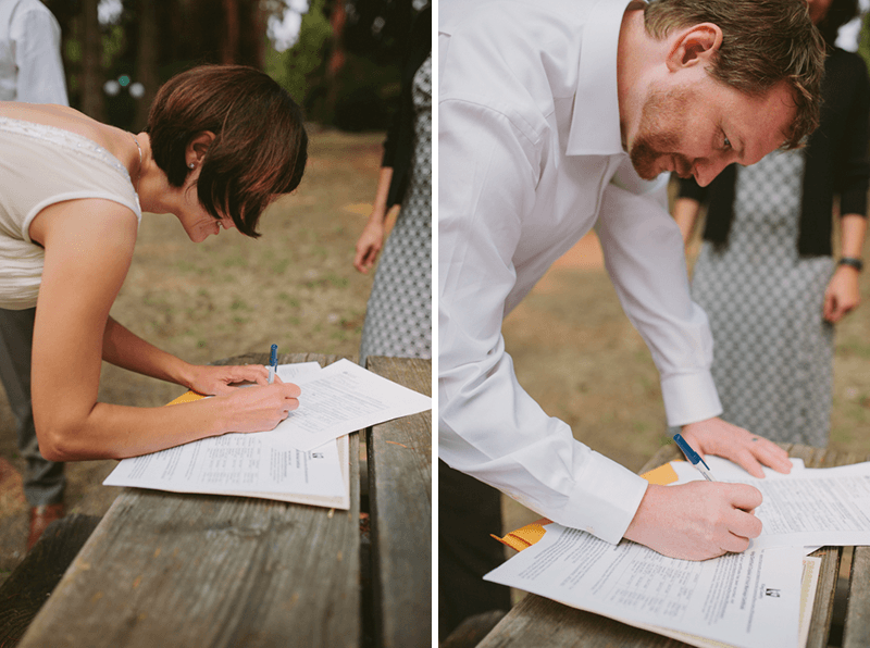 Bride and groom signing marriage license on a rustic park table. 