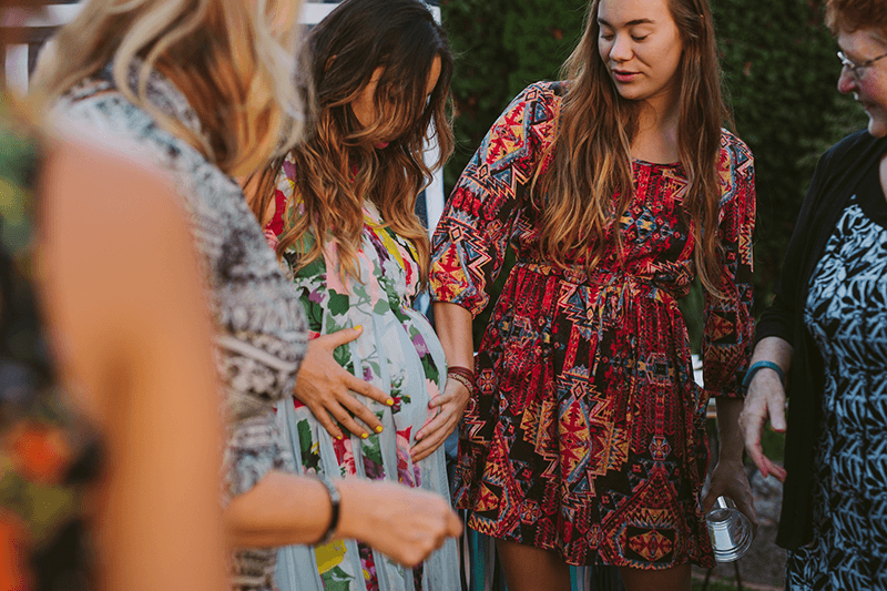 Loved ones touch a pregnant mom's belly at a baby shower. 