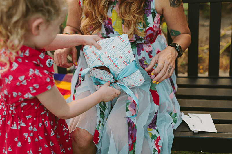 Little girl helping open presents at a summer baby shower. 