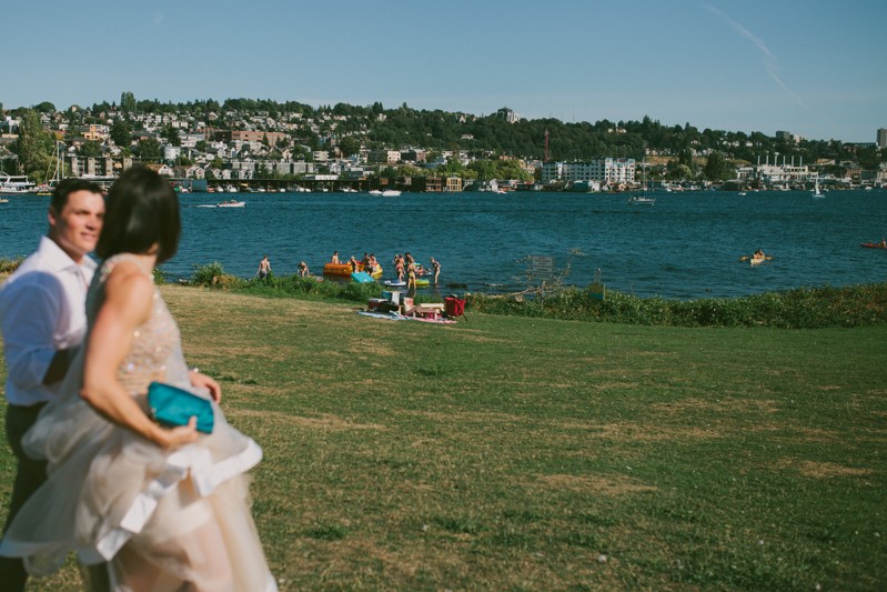 Bride and groom walk past swimmers at Gas Works Park. 