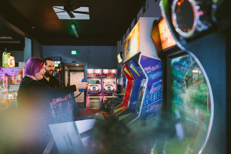 Modern engagement session in an arcade, with bride and groom playing video games. 