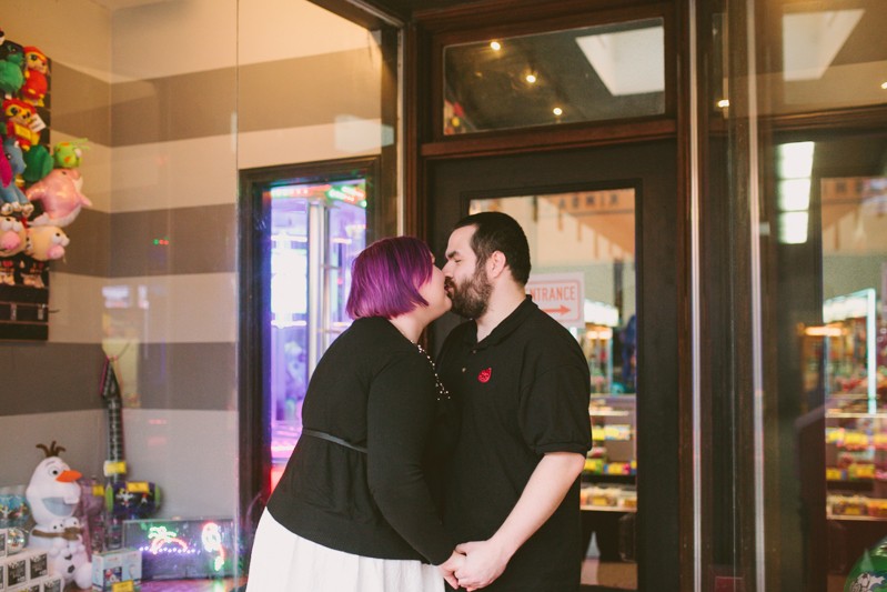 Non-traditional engaged couple kissing at Quarters Arcade in Bremerton. 