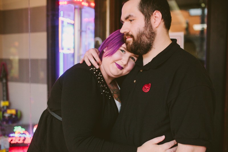 Non-traditional bride with purple hair and lipstick, hugging her groom during their fun engagement session. 