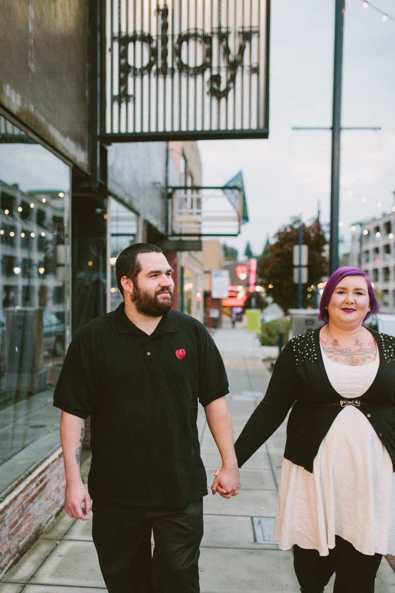 Modern, alternative engaged couple walking through downtown Bremerton, holding hands. 