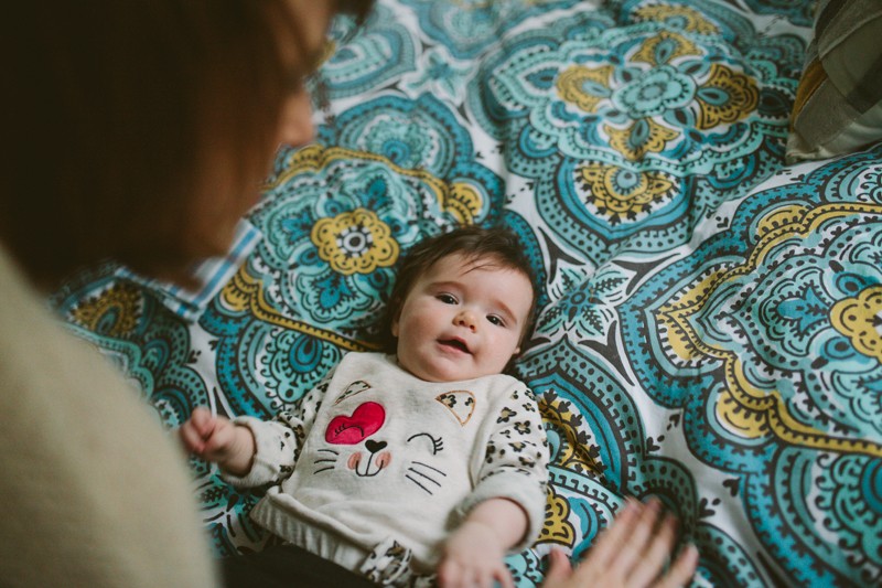 Adorable baby girl in a kitty cat sweater, laying on a modern patterned comforter at home. 