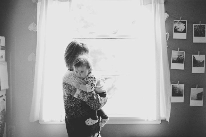 Indie lifestyle portrait session at home, with mom holding her baby and looking out a window in Kitsap County. 