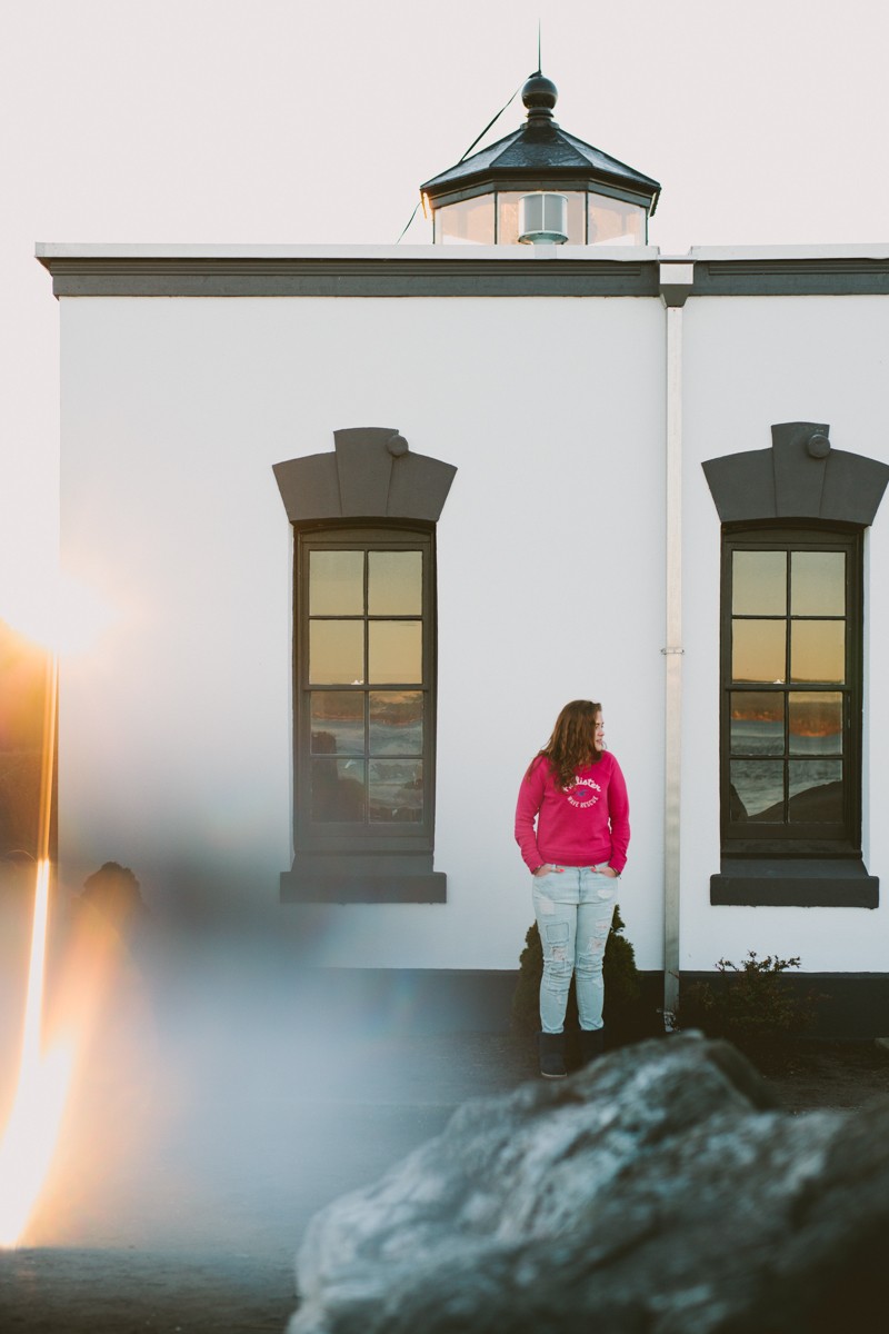 Creative high school senior photography, with girl in a pink shirt standing at a lighthouse in Hansville, WA. 
