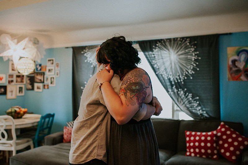 Modern tattooed couple, hugging, at home, during a lifestyle portrait session. 