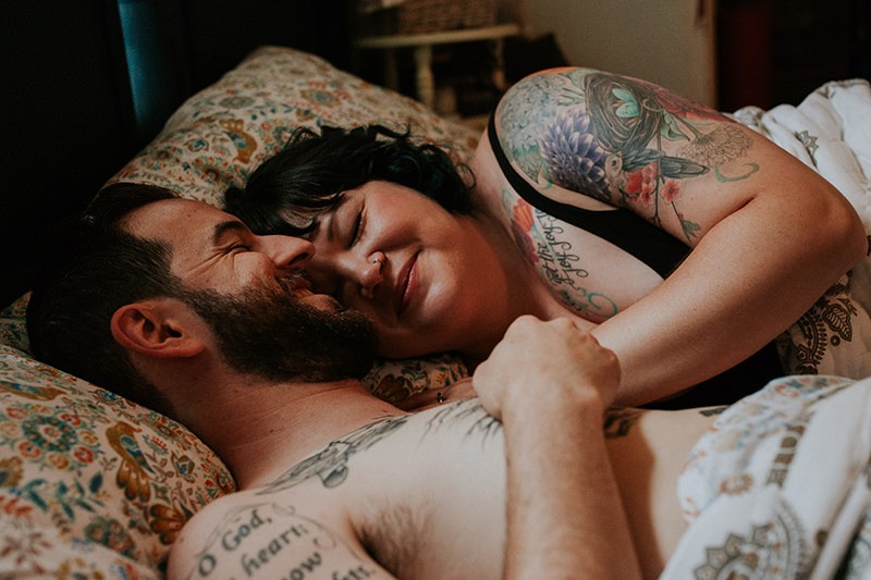 Sweet tattooed couple cuddle in bed, at home, for an intimate portrait session in Bremerton, WA. 