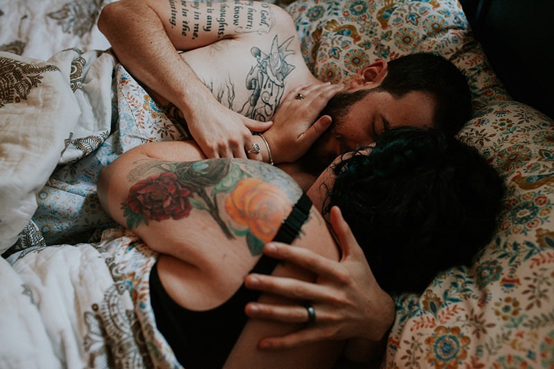 Sweet moments during a cuddly couples portrait session, with tattooed couple in bed. 