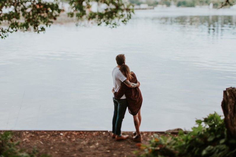 Tattooed couple cuddles on the Bainbridge Island waterfront for a lifestyle portrait session. 
