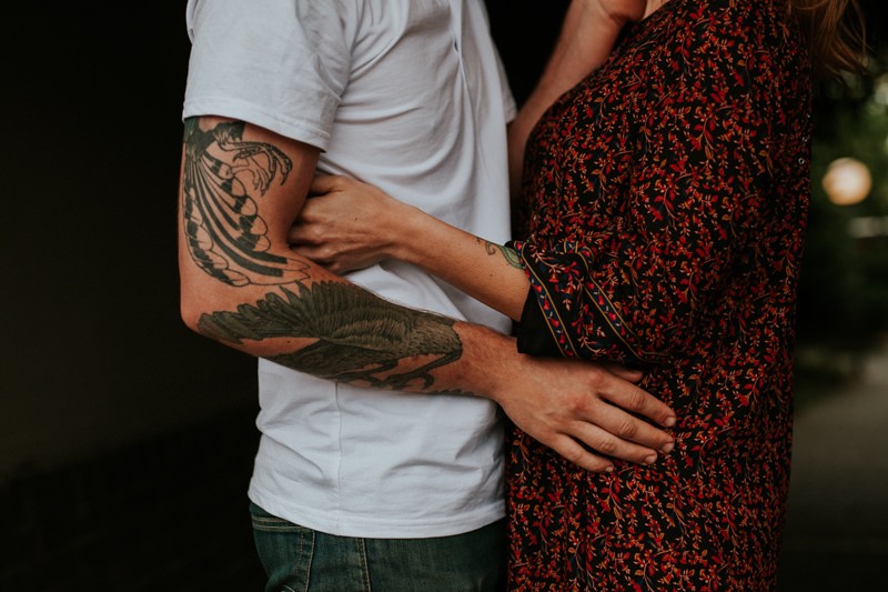 Tattooed couple in love, hugging each other, with man in a plain white t-shirt and woman wearing a floral print boho dress. 