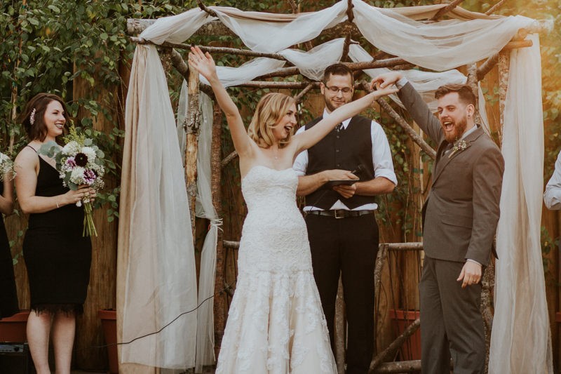 Celebratory bride and groom under a rustic wooden arch, celebrating their nuptials. 