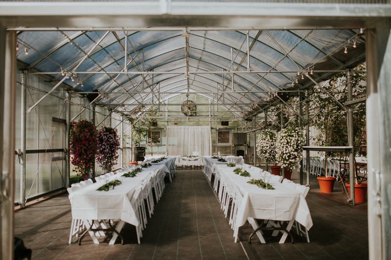 Garden wedding reception in a greenhouse, with long rectangular tables and white linens. 