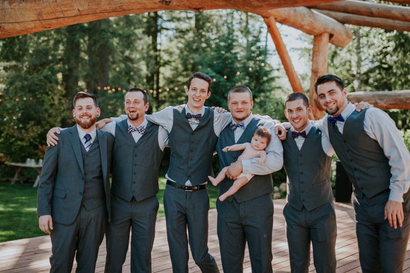 Groom and groomsmen wearing grey vests and purple ties and bow ties for a summer garden wedding. 