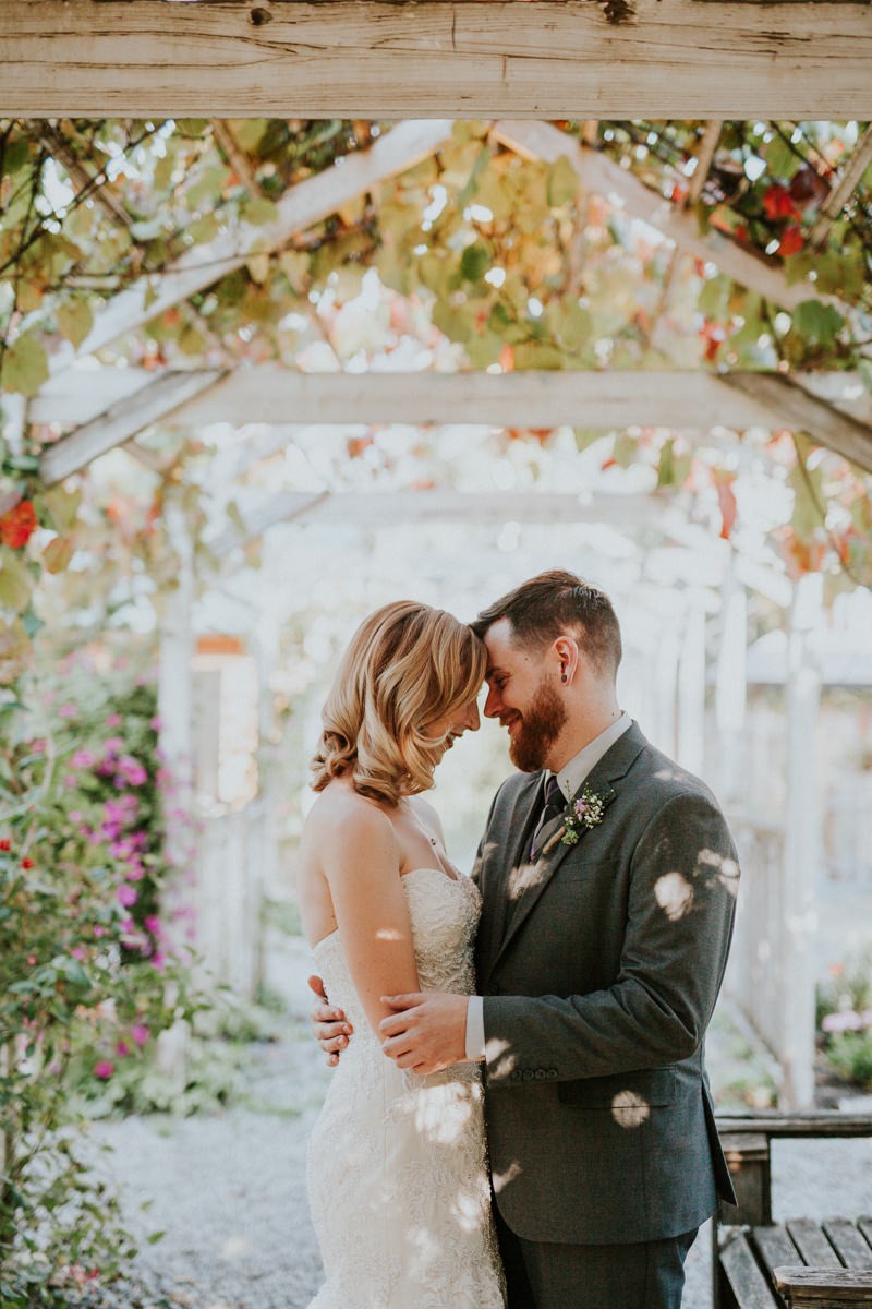 Bride and groom hugging under a garden trellis, with bride in a strapless dress with a classic shoulder-length hairstyle. 