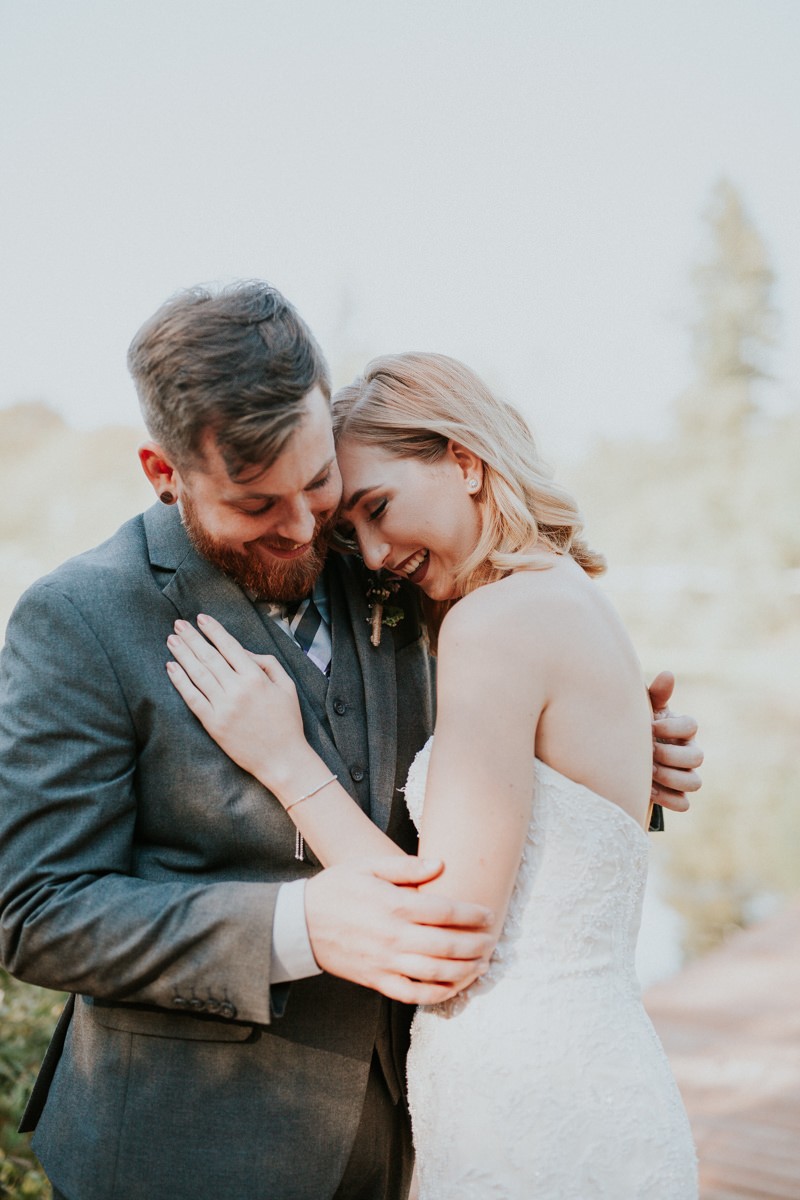 Modern bride with shoulder-length hair and bold makeup, hugging groom in a grey suit and vest. 