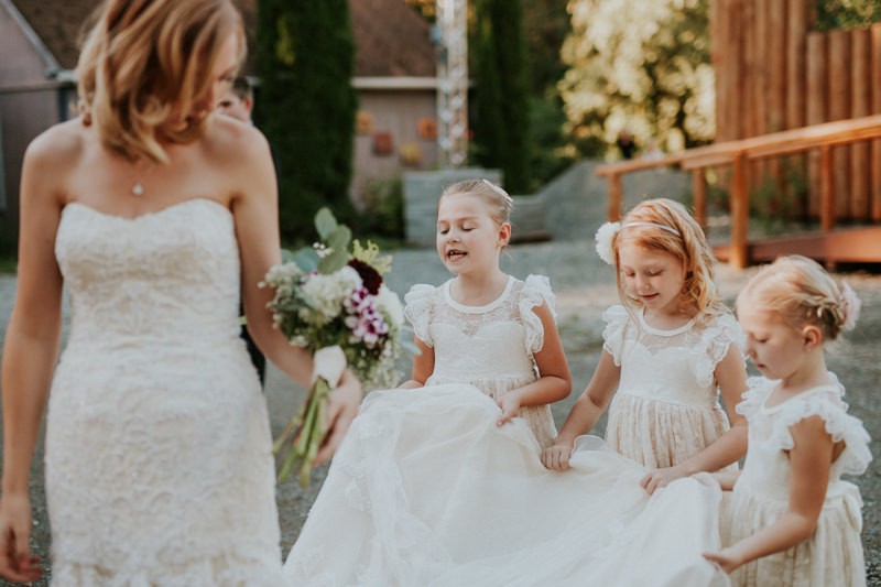 Flower girls in white lace illusion neckline dresses, holding bride's dress train. 