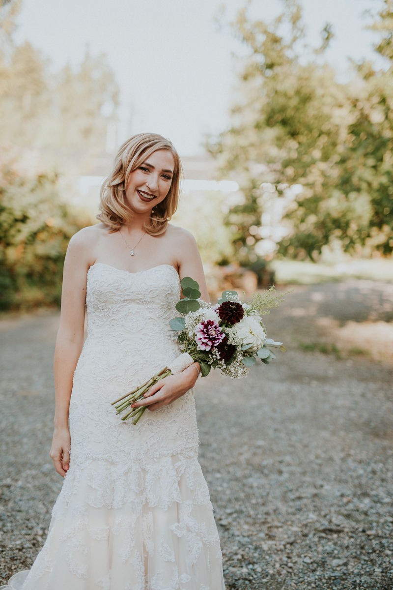 Garden glam bride in a strapless, beaded, trumpet dress, holding a bouquet of white and purple Dahlias. 