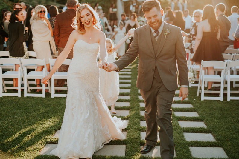 Modern bride and groom dance as a ceremony exit, while the sun sets and guests celebrate. 