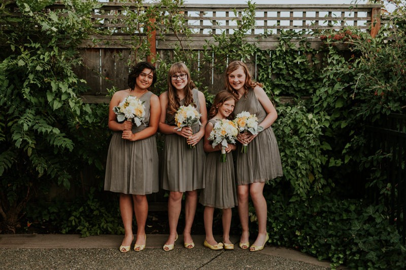 Junior bridesmaids wearing modern grey dresses, with white and yellow bouquets. 