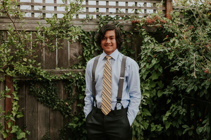 Junior groomsman wearing a blue shirt, grey suspenders, and a striped yellow tie. 