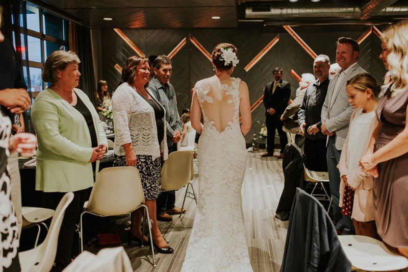 Bride walks down the aisle in modern venue, The Pine Room, as guests smile. 