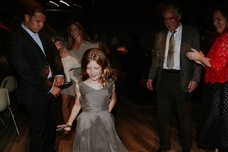 Junior bridesmaid in a modern pleated, grey dress, dancing it up on the dance floor. 