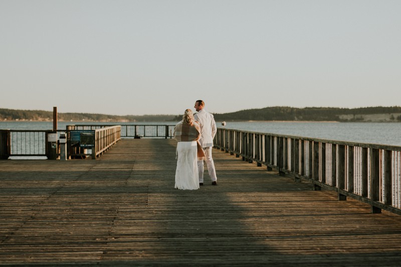 Bride and groom walk down a dock on the Port Townsend waterfront at sunset. 