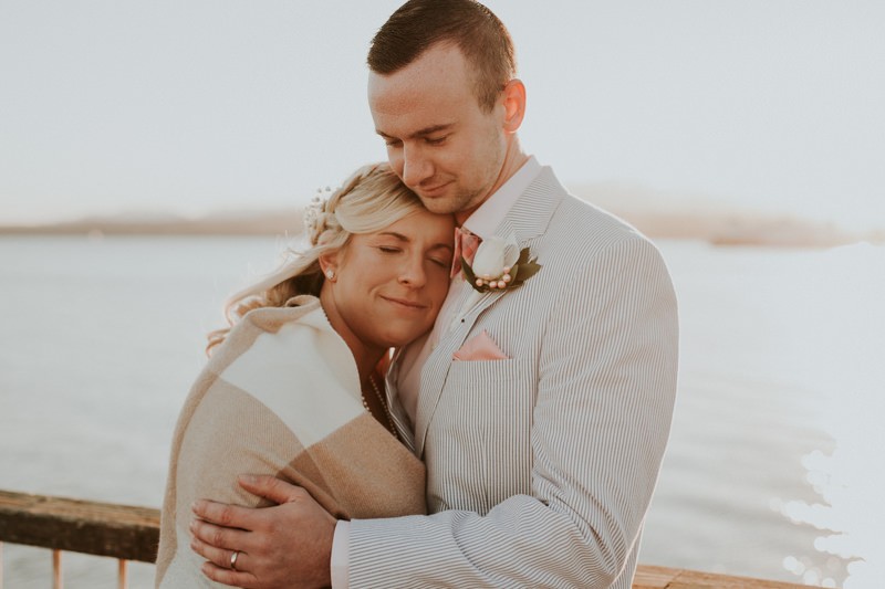 Sweet bride and groom on the Port Townsend waterfront, with groom wearing a light blue suit and coral bow tie and pocket square. 