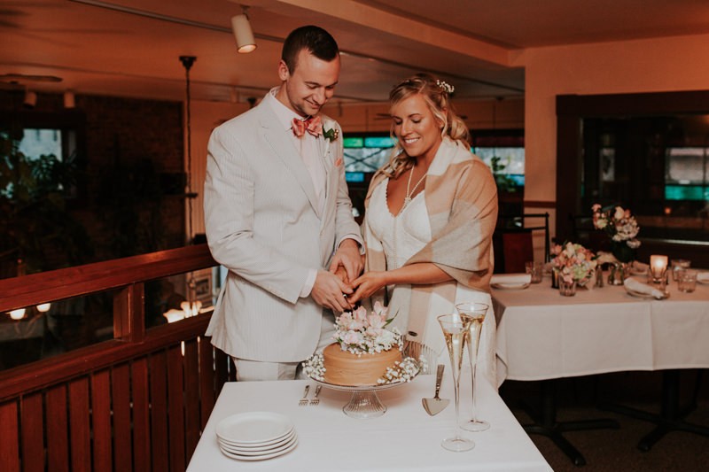 Small elopement reception with bride and groom cutting a simple one-tier frosted cake, in Port Townsend, WA. 