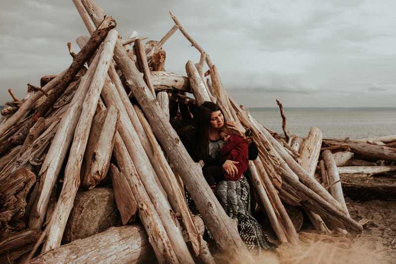 Lifestyle portrait session with a family sitting in a driftwood shelter. 