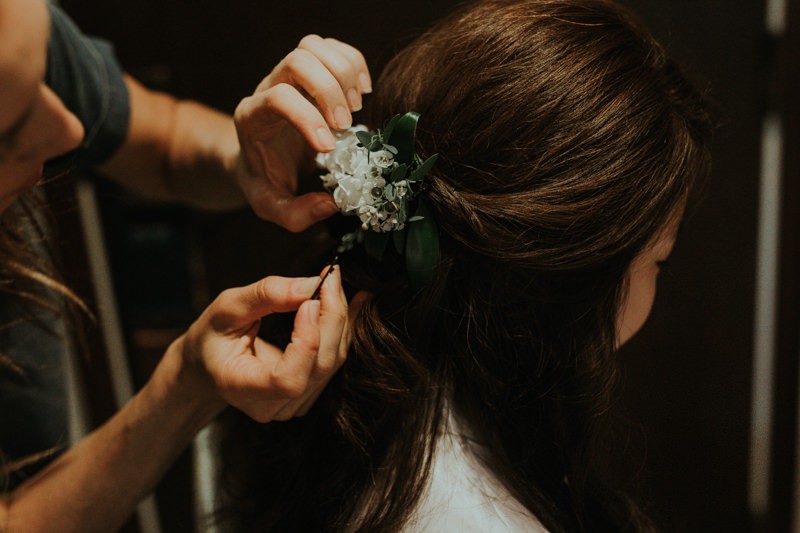 Hairstylist applying fresh floral hairpiece to bride's half updo. 