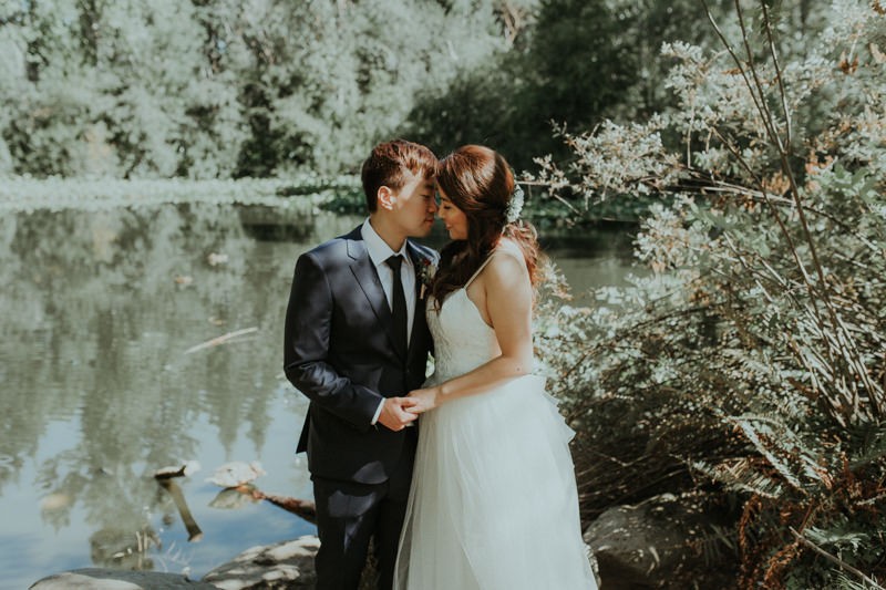 PNW bride and groom near a pond, with bride in a tulle skirt dress and groom in a dark blue suit. 